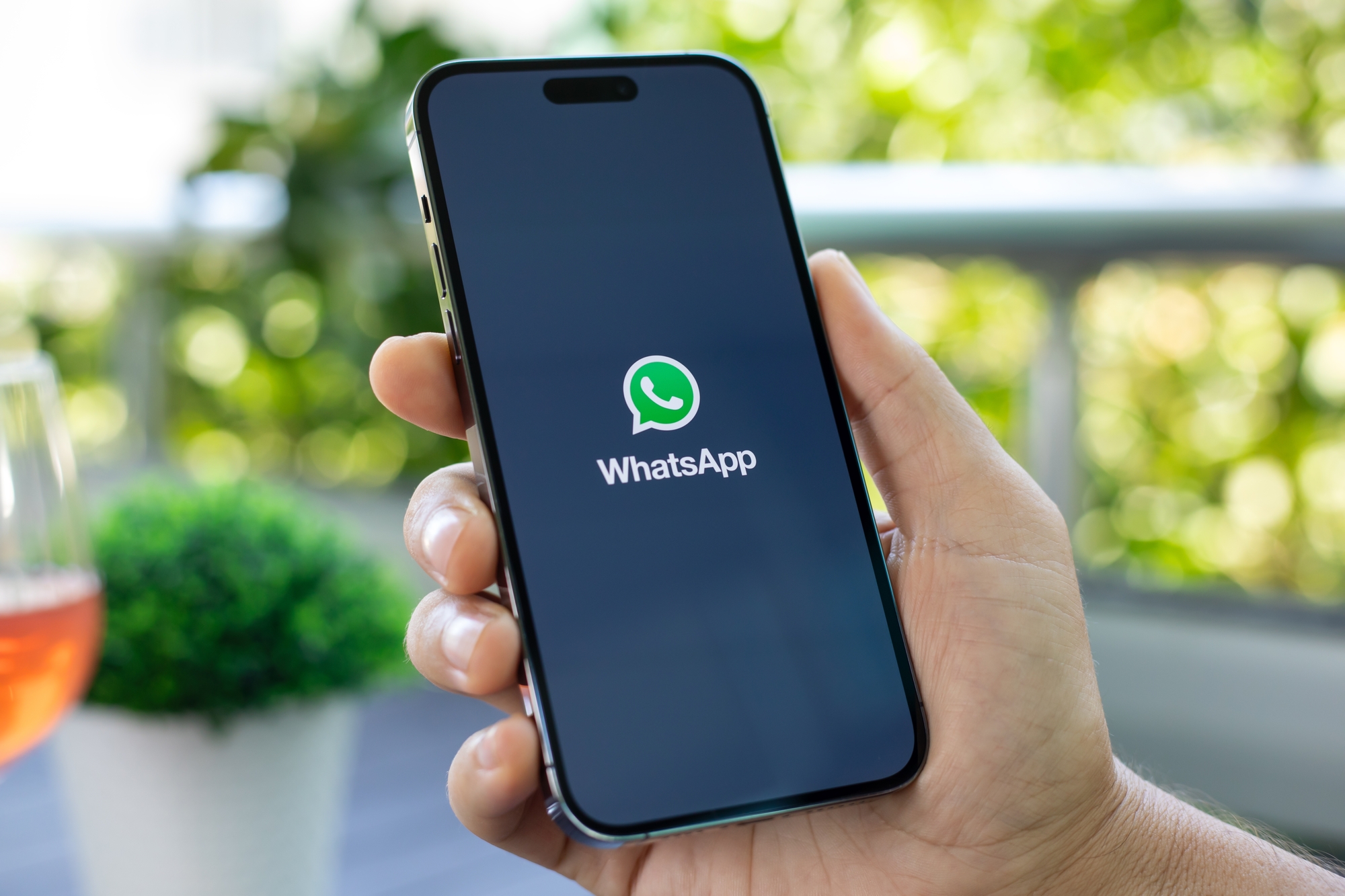 Eine Hand hält ein Smartphone mit sichtbarem WhatsApp-Logo vor unscharfem Hintergrund.
